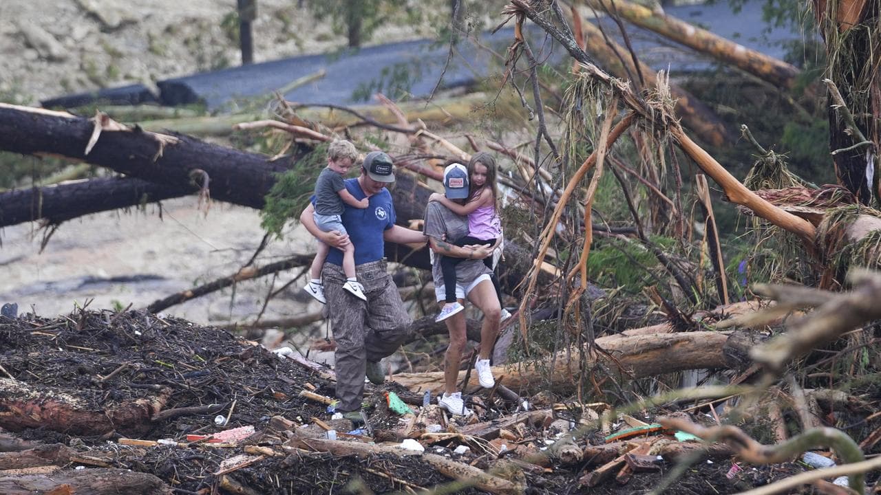 People climb over debris on a bridge over Guadalupe River