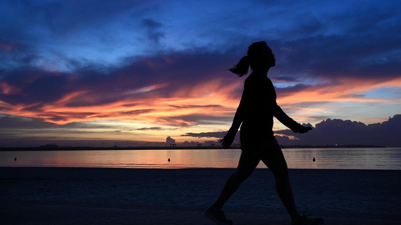 A woman walks along Brighton-Le-Sands Beach at sunrise in Sydney