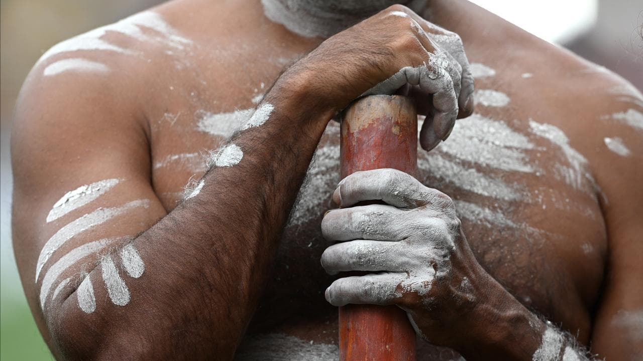 an Indigenous Australian man holding a Didgeridoo