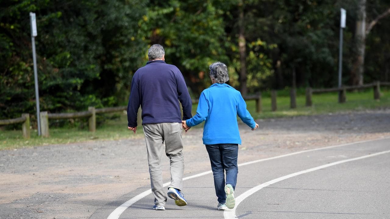 An elderly couple walk through a park