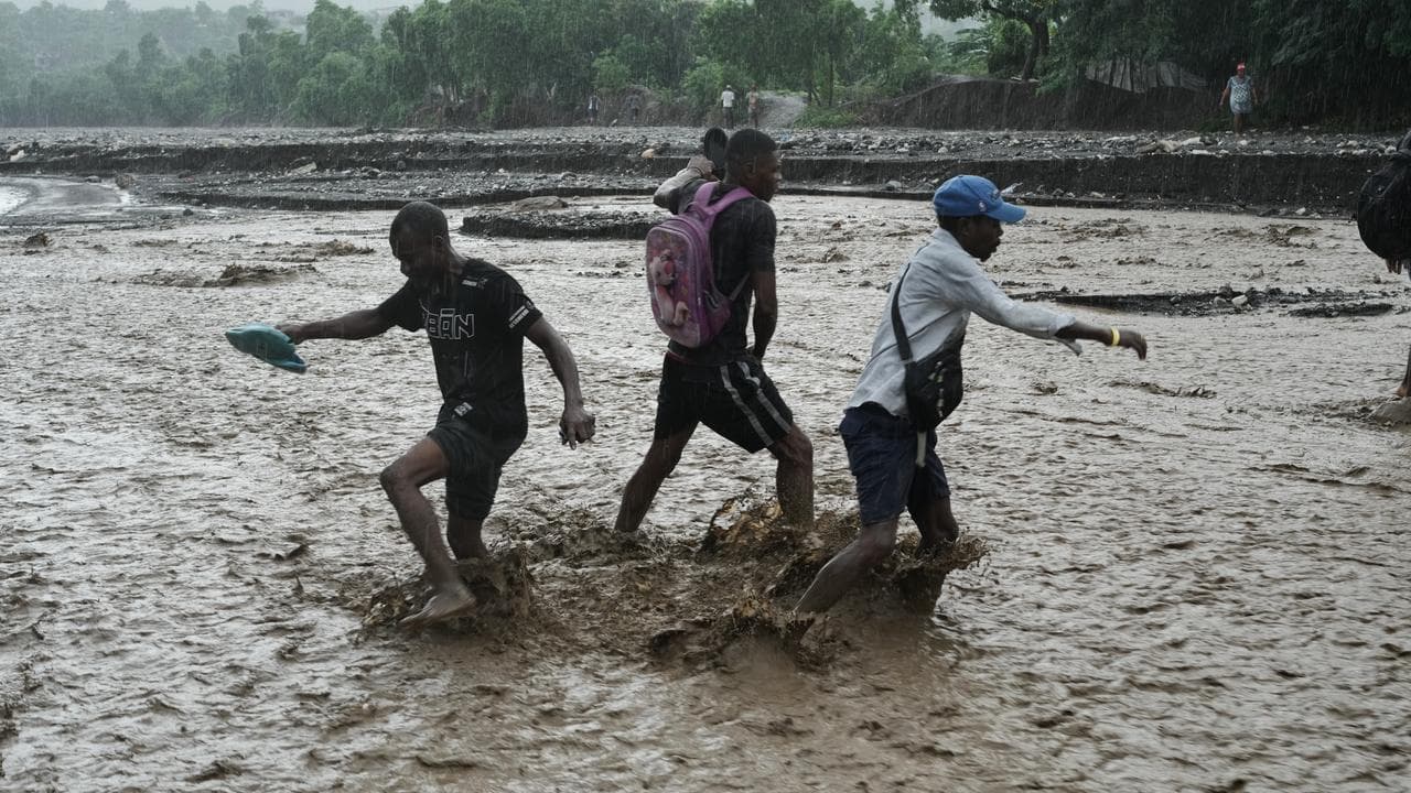 Residents wade through a flooded stream in Haiti