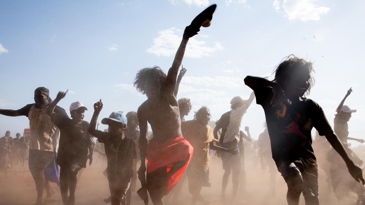A photo of Indigenous children dancing in a dusty area.