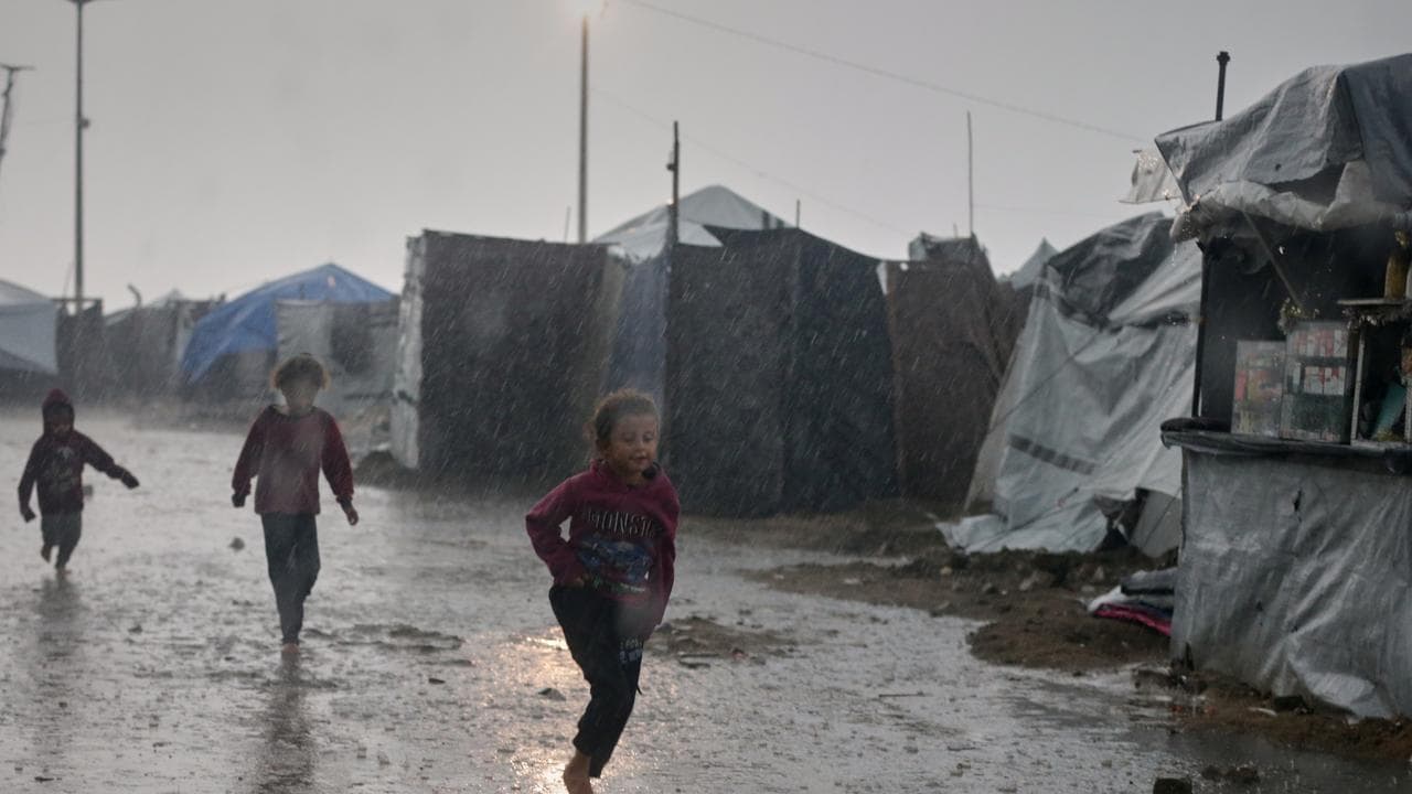 Children run in the rain past a tent camp in Gaza City