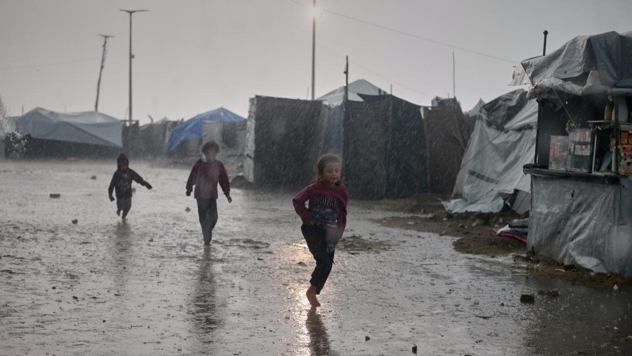 Children run in the rain past a tent camp in Gaza City