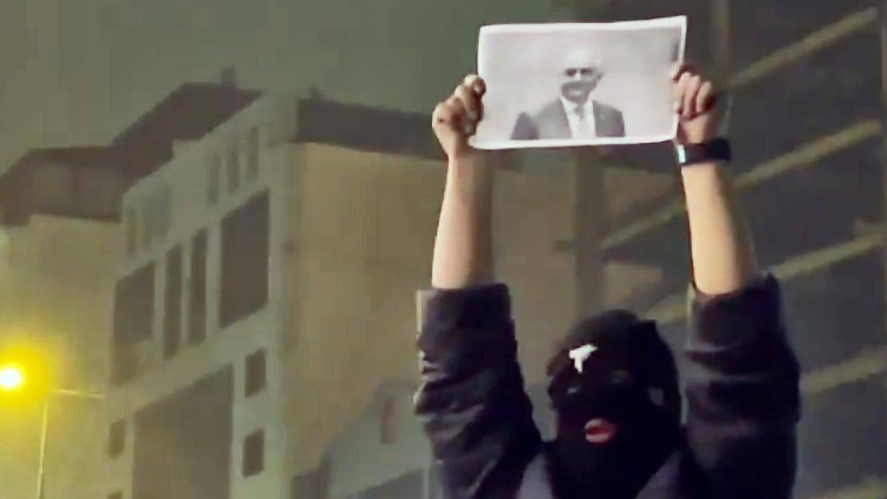 masked demonstrator holds a picture of Reza Pahlavi